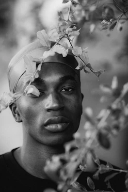 Black and white portrait of Nancy with a serene expression, framed by sage green leaves.