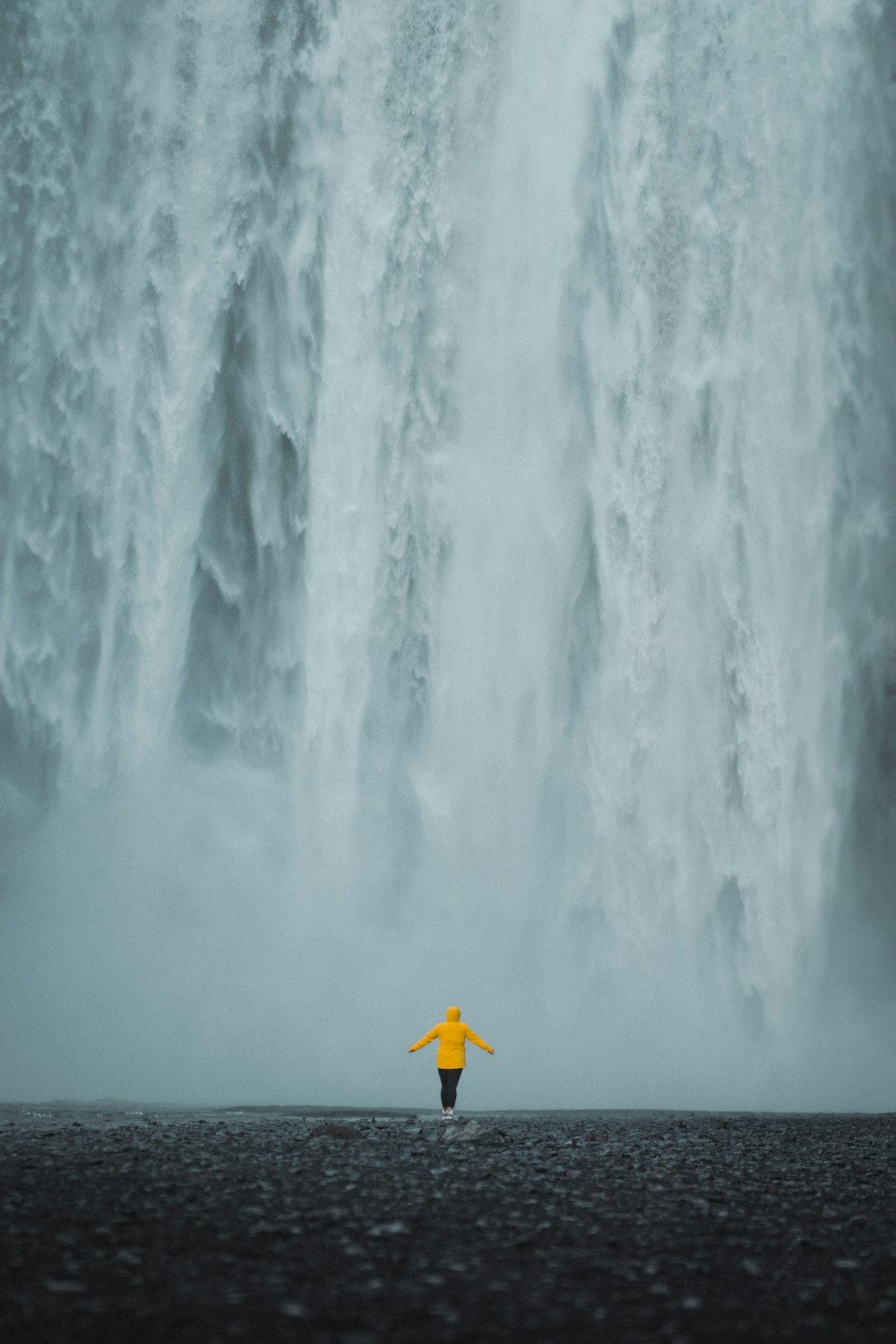 eine Person mit einem gelben Regenschirm, die vor einem Wasserfall steht