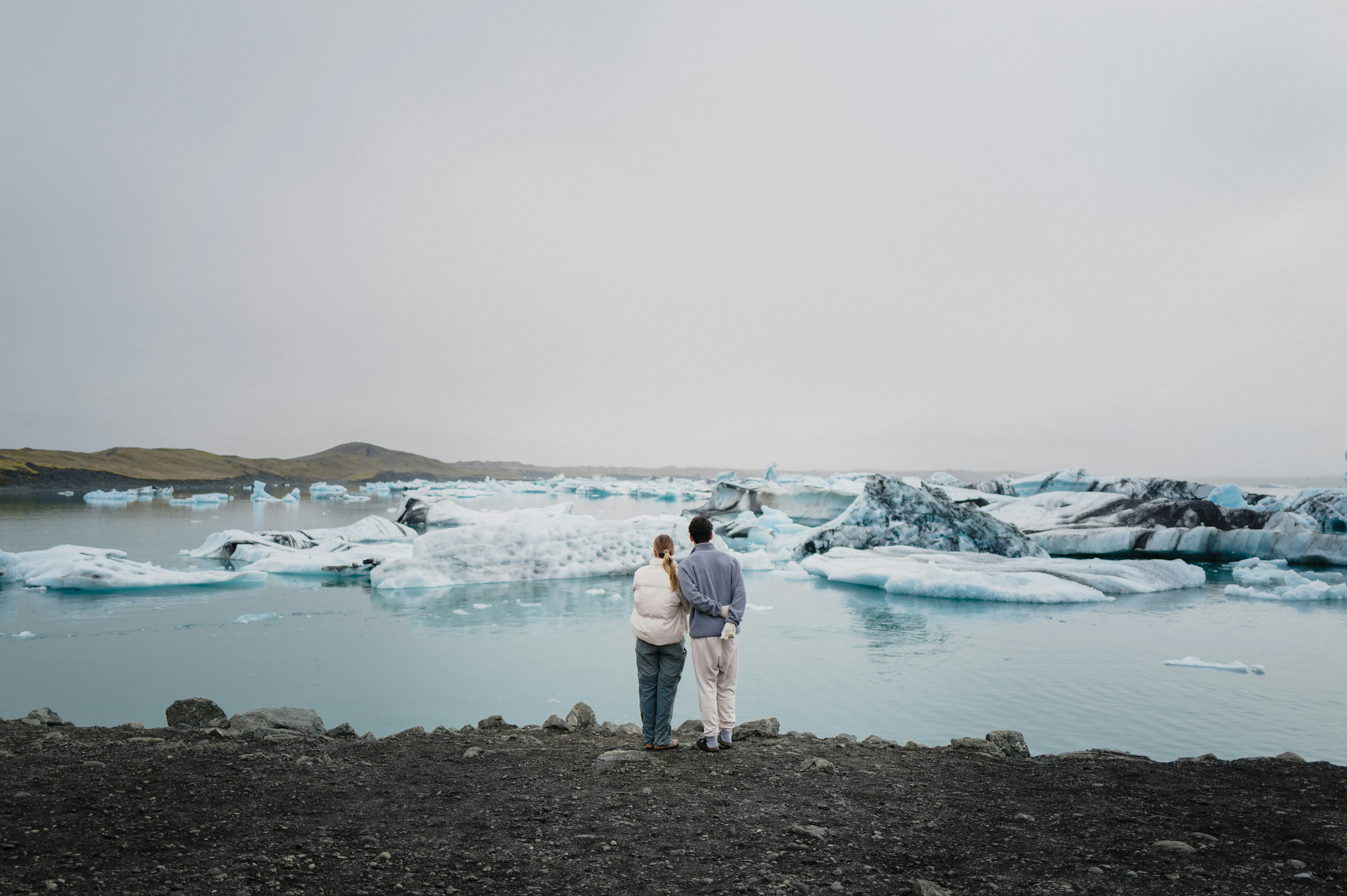 a man and a woman standing in front of a body of water, in awe