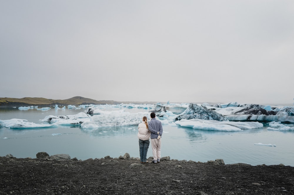 a man and a woman standing in front of a body of water