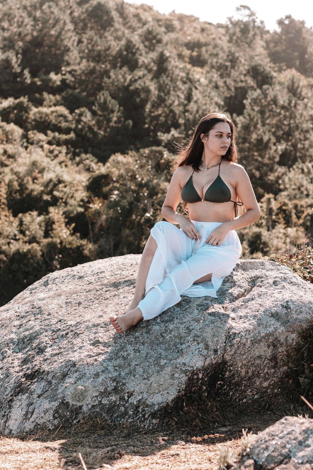 a woman in a bikini top sitting on a rock