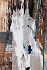 A textured and abstract composition featuring a mix of vertical and horizontal strokes. The image includes layers of earthy tones with splashes of white, blue, and turquoise brush strokes, creating a dynamic interplay of colors and textures.