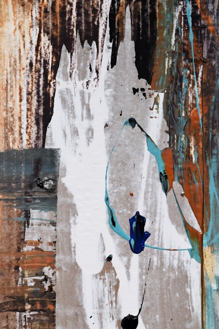 A textured and abstract composition featuring a mix of vertical and horizontal strokes. The image includes layers of earthy tones with splashes of white, blue, and turquoise brush strokes, creating a dynamic interplay of colors and textures.