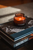 A warm, golden-hour photo of a lit candle resting beside a stack of well-loved books on a wooden table.