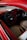 A vintage car interior with a retro-styled steering wheel and dashboard. The seats have a quilted pattern with red and beige colors, and the door panels are detailed with artistic accents.