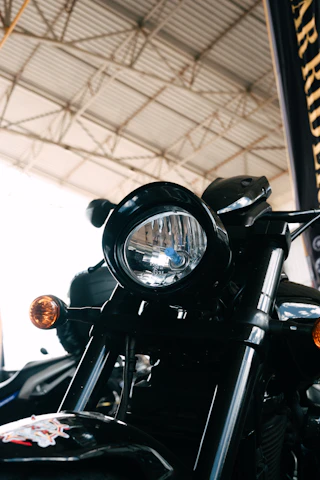 Close-up of a sleek custom motorcycle headlamp glowing softly in a dark garage with red and black accents.