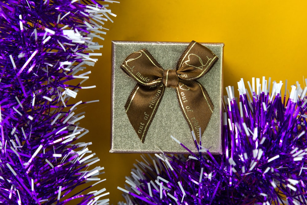 a gift wrapped in brown ribbon sitting on top of a purple christmas tree