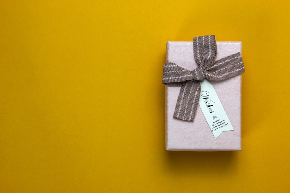 Una caja de regalo envuelta con una cinta sobre un fondo amarillo