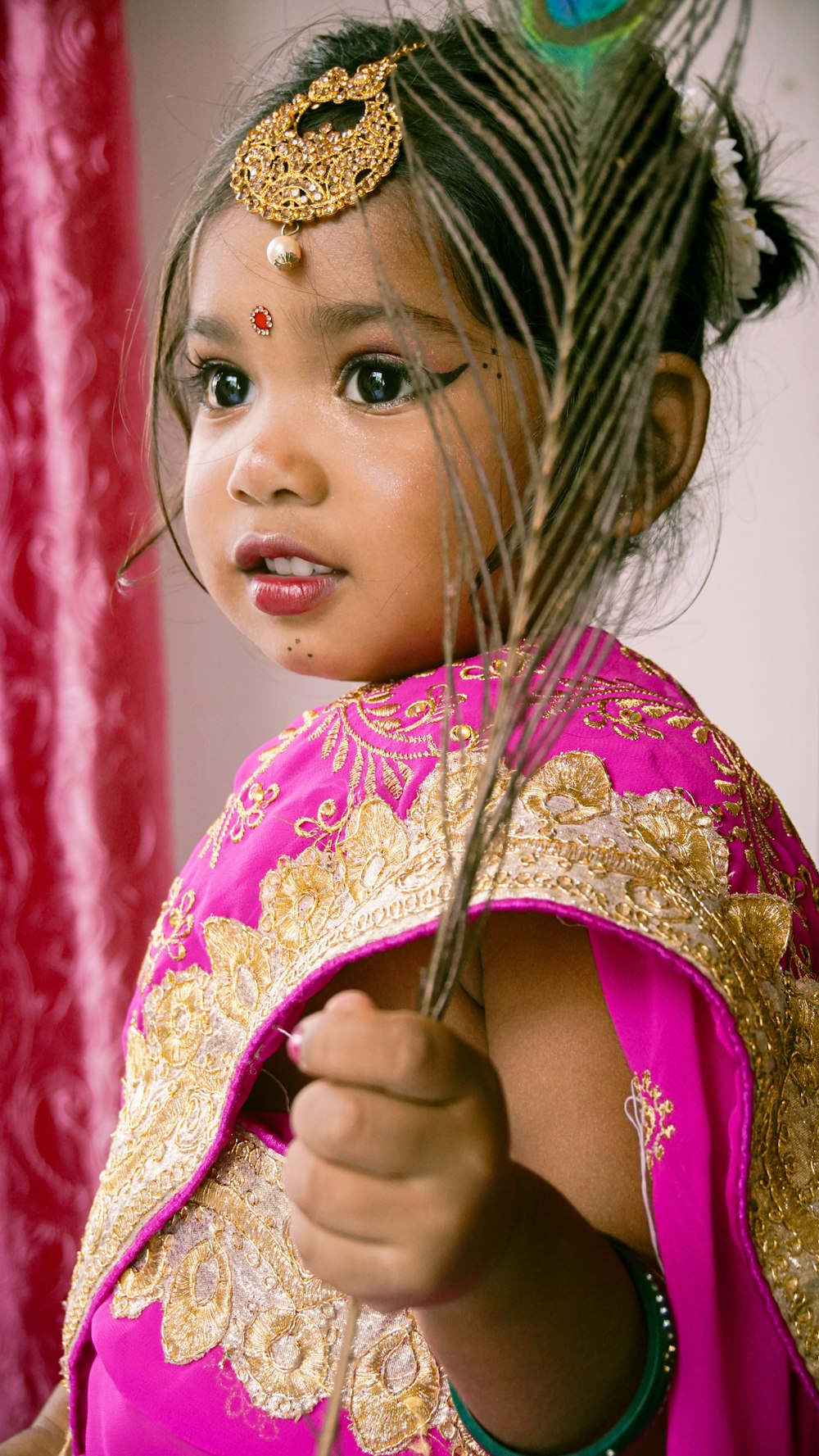 a little girl in a pink dress holding a feather