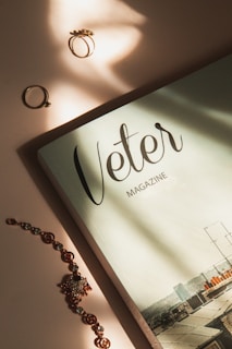 A magazine titled 'Veter' is placed on a flat surface, accompanied by rings and a decorative bracelet with intricate designs. The lighting is soft and creates gentle shadows on the objects.
