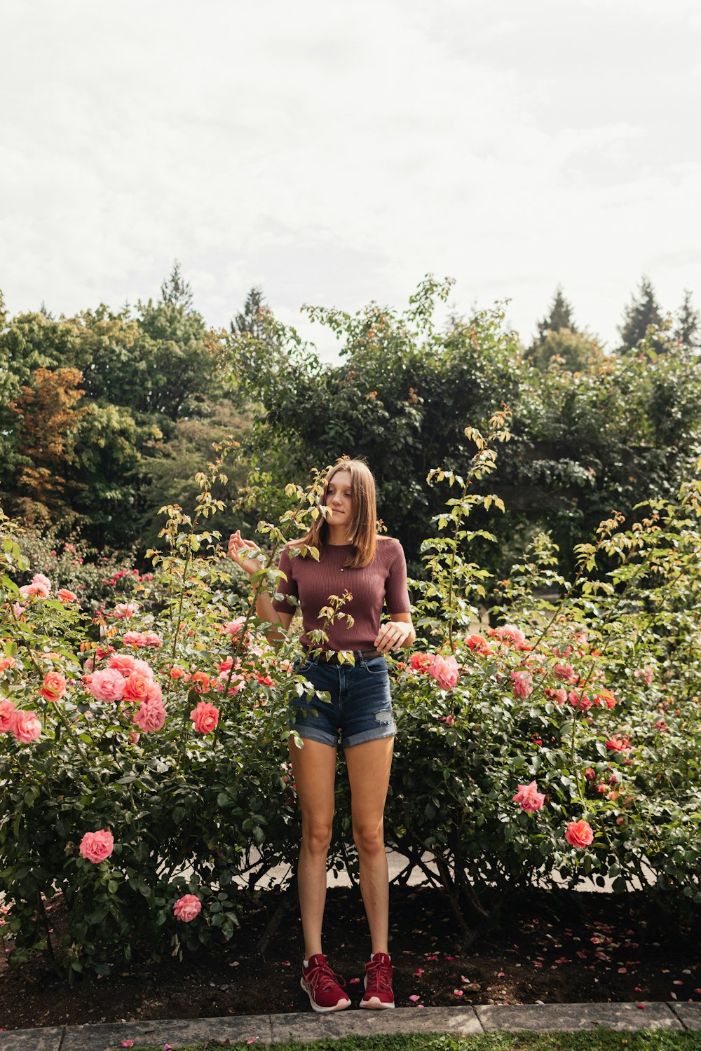 a woman standing in front of a bush of flowers