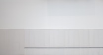 A minimalist, abstract wall with a monochromatic color palette, featuring a horizontal line near the bottom. The surface is smooth and evenly divided into sections, giving it a structured and uniform appearance.