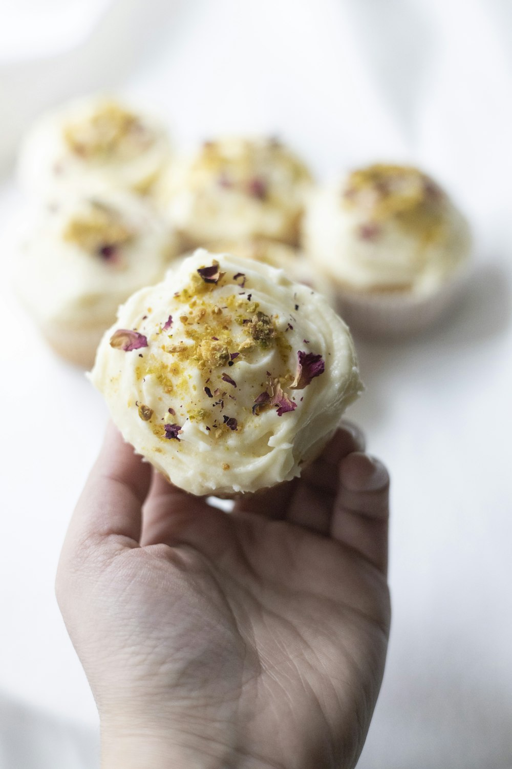 a hand holding a cupcake with white frosting and sprinkles