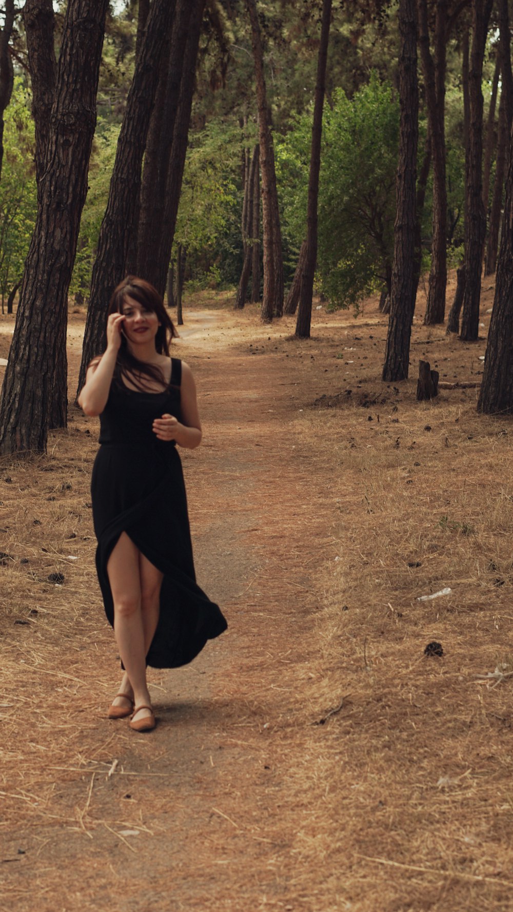 a woman in a black dress walking through a forest
