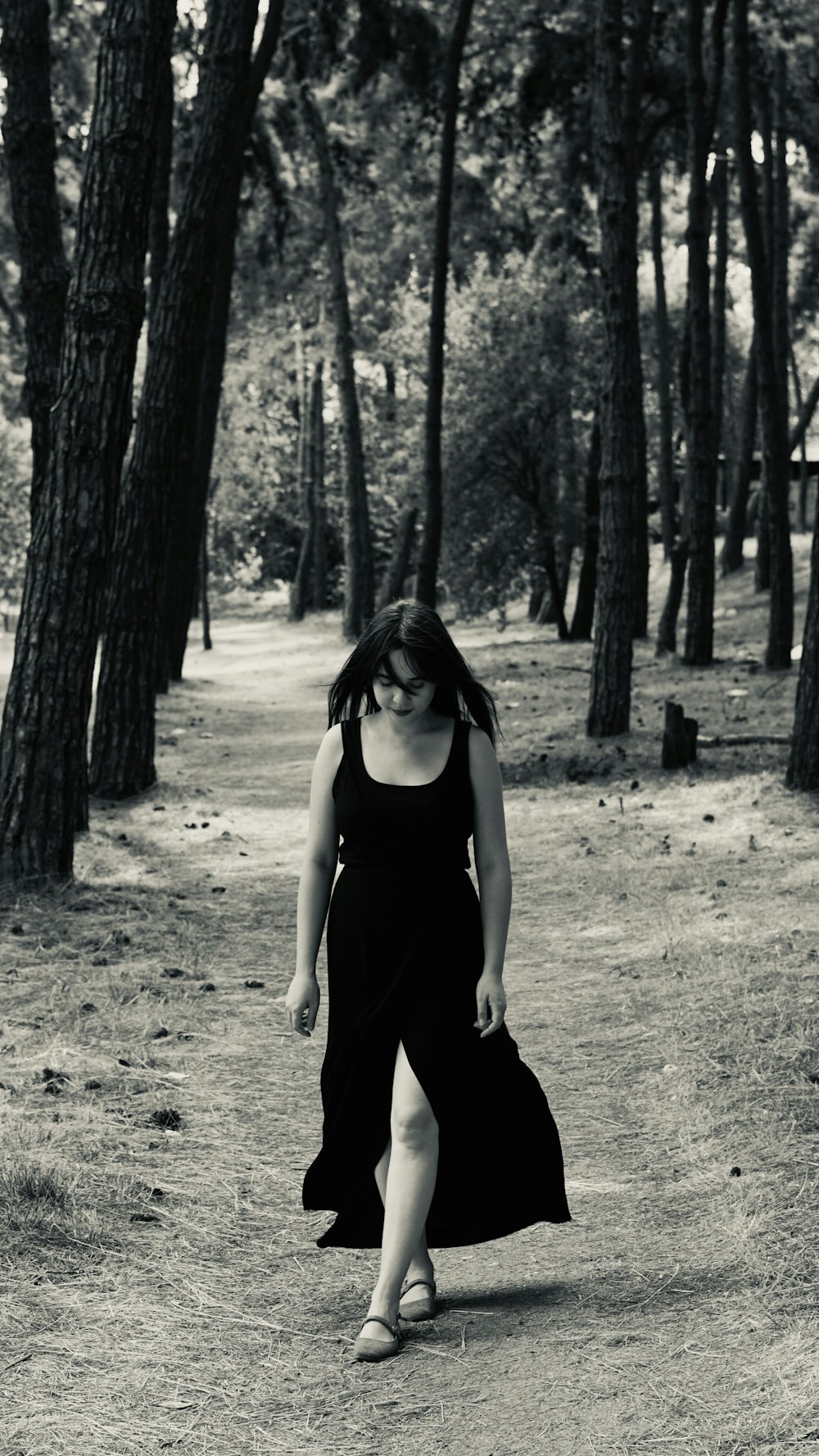 a woman in a black dress is walking through the woods