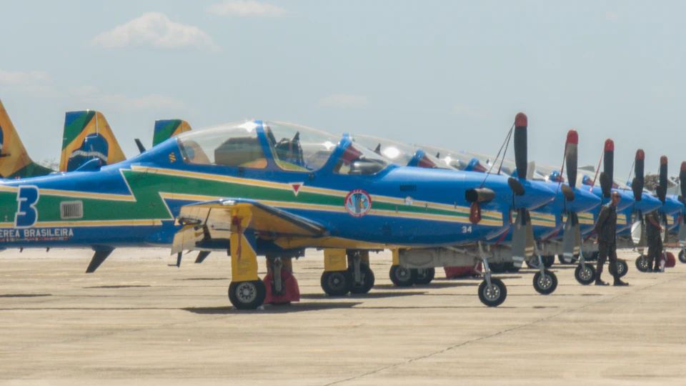 Nine identical blue and yellow airplanes line up on tarmac with propellers spinning
