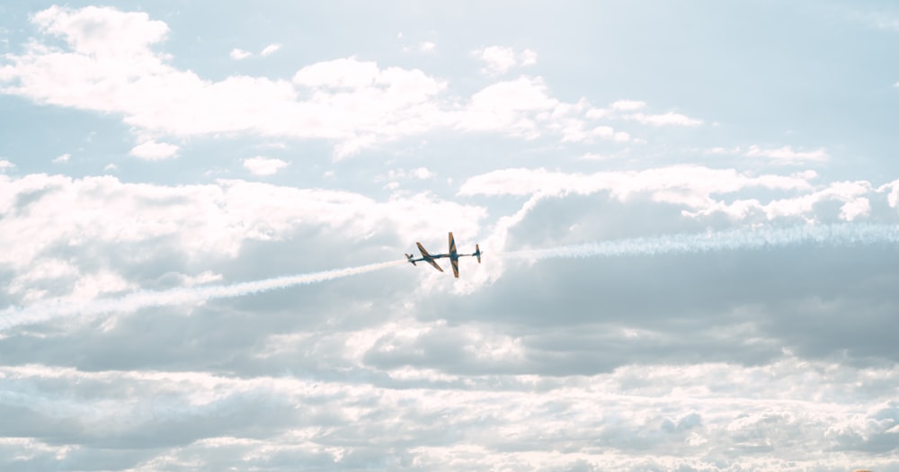 a plane flying through a cloudy sky with contrails