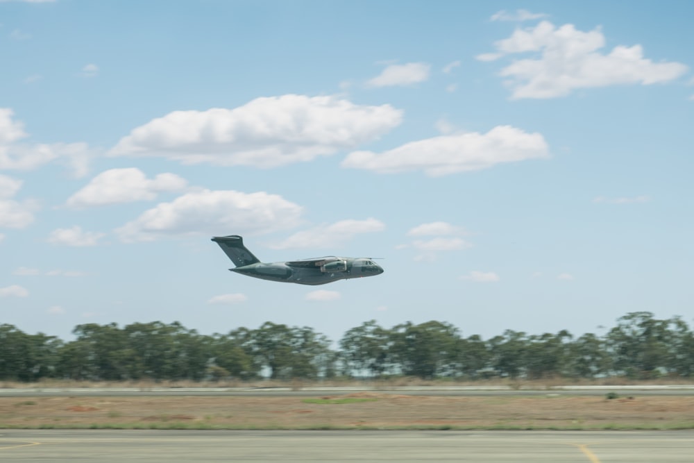 a plane flying low over a runway with trees in the background