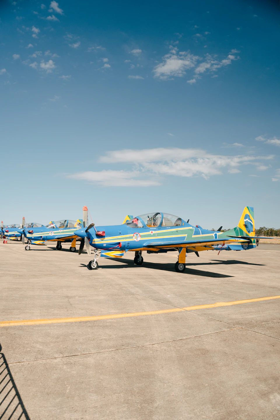 Four blue and yellow airplanes parked on an airfield under clear blue sky with white
