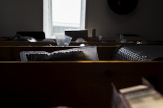 Several sealed bags filled with legumes or seeds are displayed on a wooden counter. Light from a window illuminates the scene, while woven materials and miscellaneous objects are visible in the background, adding to the rustic ambiance.