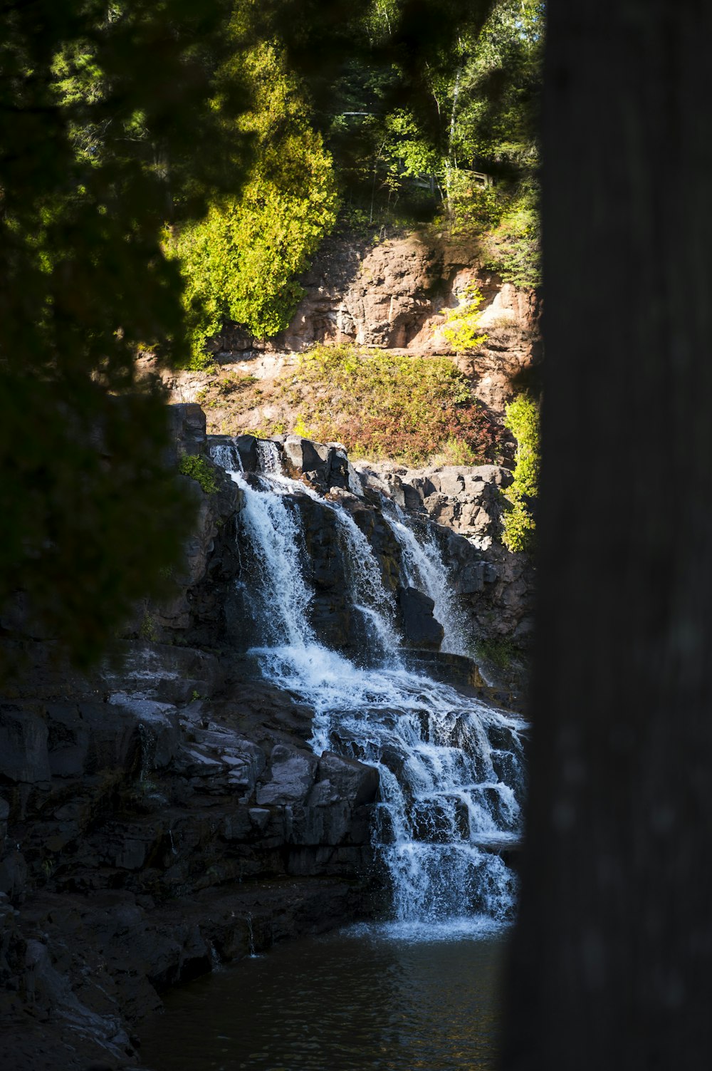 a waterfall is seen through the trees near a body of water