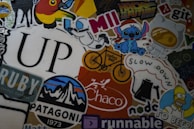 A colorful collage of various stickers featuring different designs, including a space-themed character, cartoon figures, a stylized mountain logo, coffee-themed graphics, and the word 'UP' in large font. There are references to popular culture, nature, and coding. Some stickers contain text, such as 'Hack to the Future,' 'Patagonia,' 'Coffee Ride,' and 'Slow Down.'