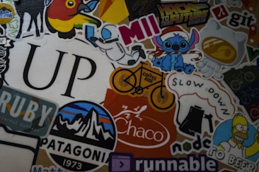 A colorful collage of various stickers featuring different designs, including a space-themed character, cartoon figures, a stylized mountain logo, coffee-themed graphics, and the word 'UP' in large font. There are references to popular culture, nature, and coding. Some stickers contain text, such as 'Hack to the Future,' 'Patagonia,' 'Coffee Ride,' and 'Slow Down.'
