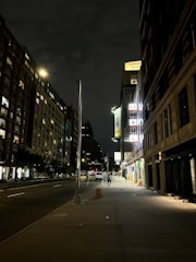 A night-time view of a moving truck parked outside a building with movers unloading furniture under bright lights.
