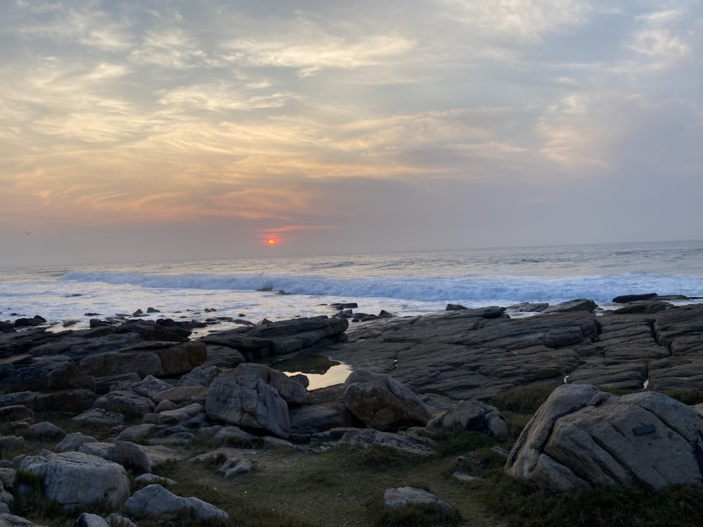 the sun is setting over the ocean and rocks