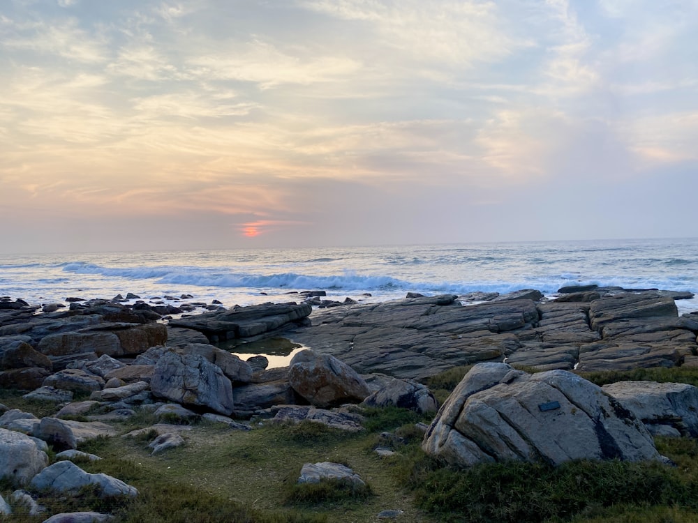 the sun is setting over the ocean and rocks