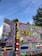 A vibrant and elaborately painted food truck with detailed artwork covering its surface. The designs include floral patterns, decorative elements, and a label reading 'FOOD TRUCK' in bold letters. There is also a sign with 'TRUCK WALL THE SPICY TRAILER' and a colorful mural featuring landscapes and intricate designs.