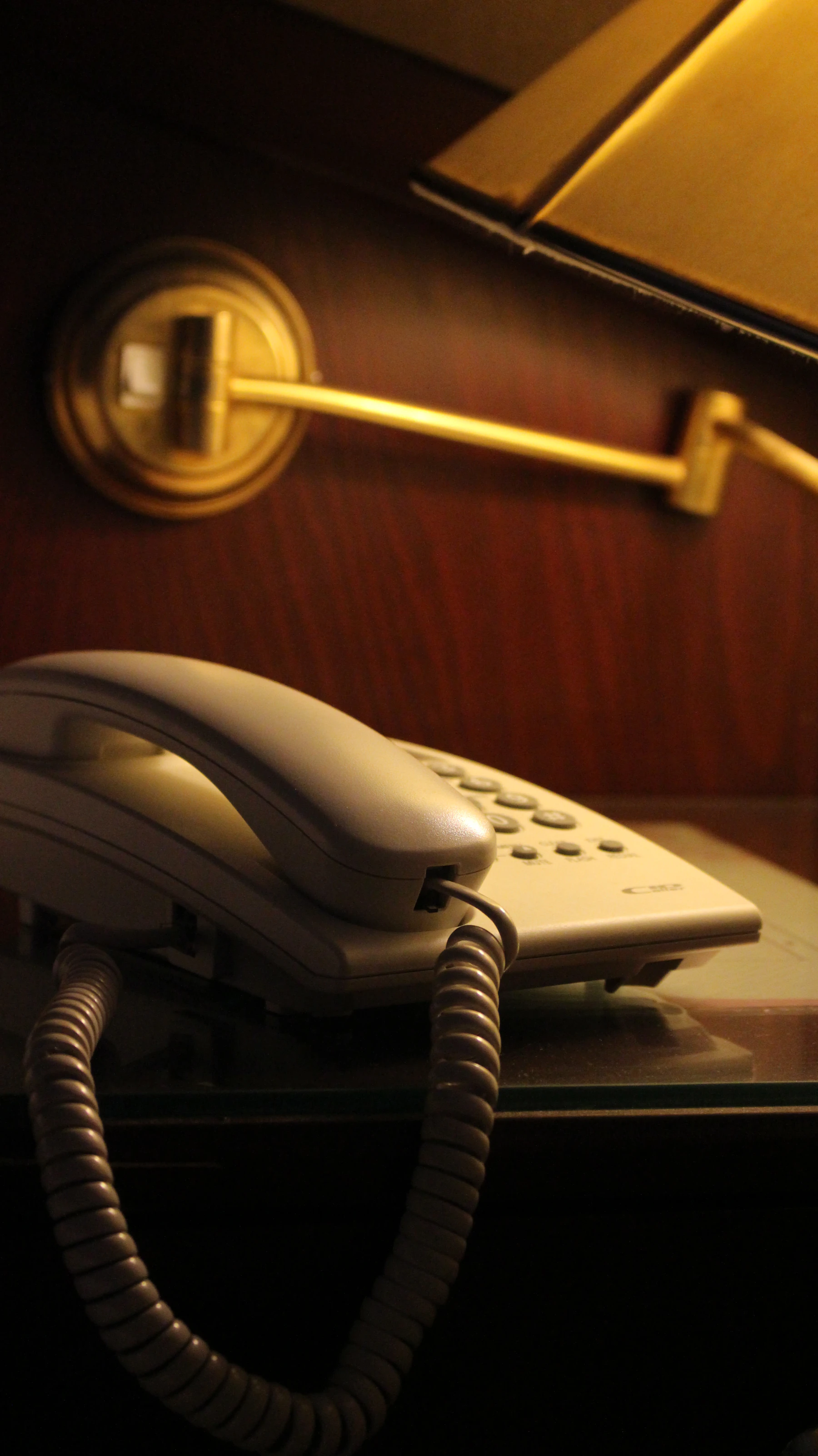 A corded telephone sits on a bedside table below a small lamp.