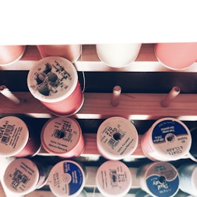 Spools of thread in varying colors are arranged on a wooden holder. Each spool is labeled with information about thread type and color. The arrangement is neatly organized and appears to be well-maintained.