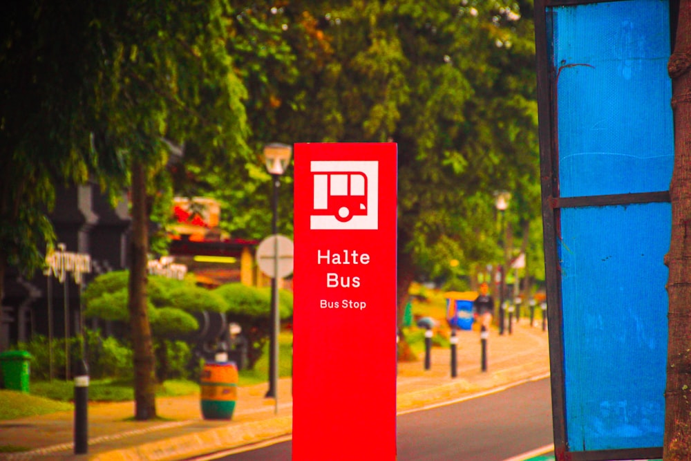 a red bus stop sign sitting on the side of a road