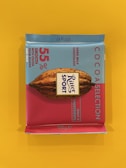 A square chocolate bar packaged in a colorful wrapper with a combination of light blue and pink colors. The branding prominently displays 'Ritter Sport' with details about the product, including '55% smooth with cocoa from Ghana and milk' and 'Dark Milk Chocolate'. A cocoa pod illustration is featured in the center.