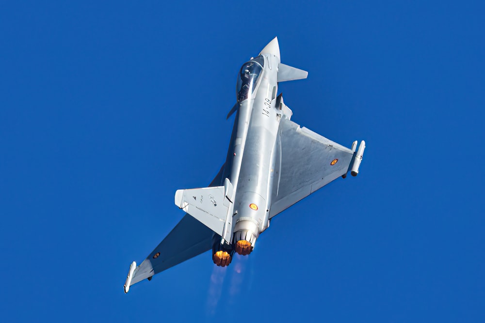 Un avión de combate plateado volando a través de un cielo azul