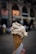 A hand holds a waffle cone with a scoop of creamy ice cream against an urban backdrop. The background is blurred, featuring a building with large windows and warm lights creating a cozy atmosphere.