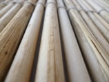 A close-up view of several bamboo sticks arranged parallel to each other, displaying a range of light brown and beige shades with visible natural textures and grains.