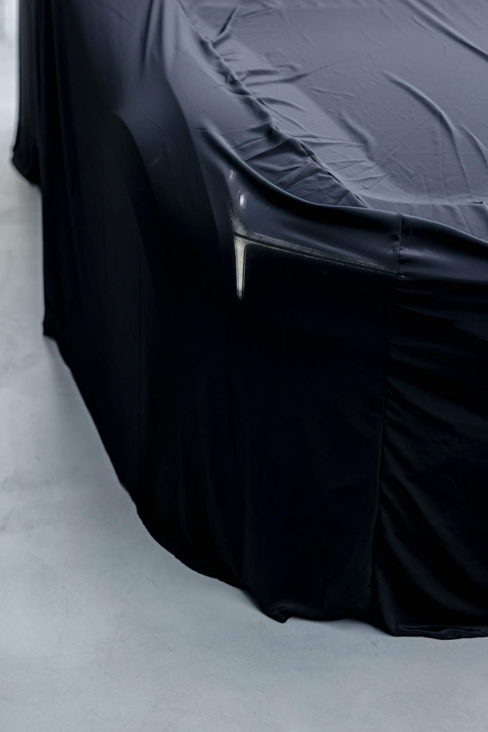 a car covered in a black cover sitting on top of a white floor