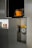 A modern-looking cabinet with a metallic finish. The cabinet has several compartments, one of which contains a brake disc with a yellow caliper. Another open compartment has a bag that is black with an orange front pocket. There are also three small items displayed in one of the compartments, which look like miniature models or packaged products.