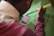 A person is using a soldering iron to work on a circuit board on a green surface. The person is wearing a maroon sweatshirt and the soldering iron has a yellow handle.