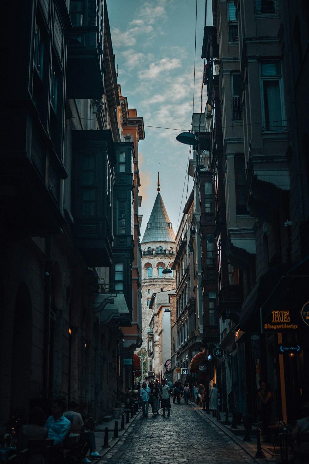 a narrow city street with a church steeple in the background