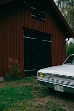 a white car parked in front of a red barn
