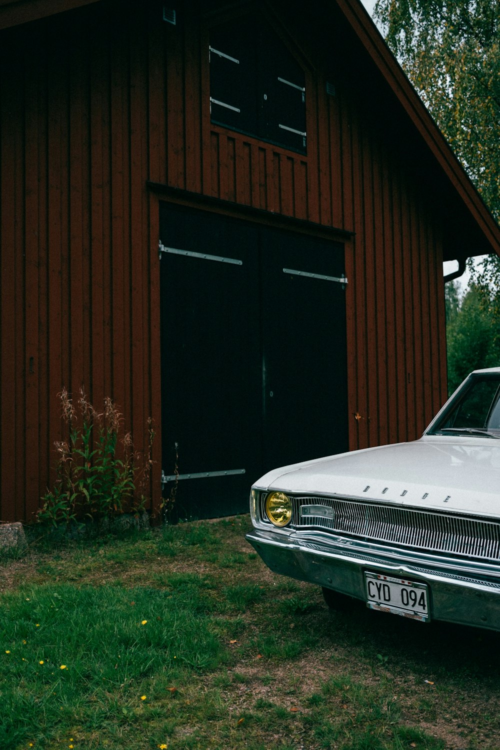 a white car parked in front of a red barn