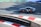 A sports car with a dark body and red wheels is racing on a track with red and white curbs. The track shows green and blue areas beyond the pavement. The car is branded with 'MASTER DRIVE' on its side.