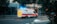 An emergency ambulance vehicle, marked 'PROTECTION CIVILE,' driving on a city street with flashing blue lights. The vehicle is white with red and yellow markings, and the surroundings include buildings and trees.