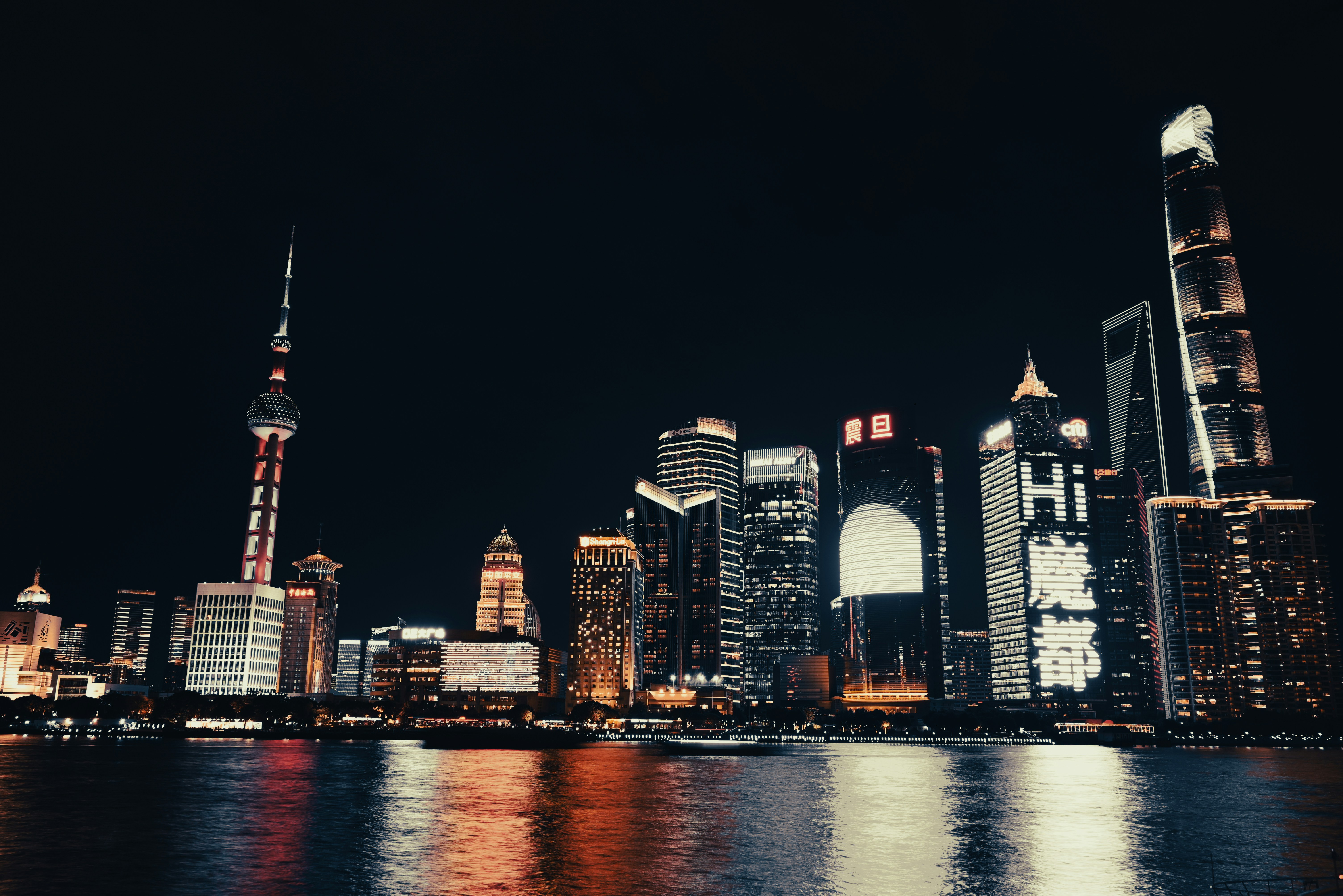 Dubai Creek Harbour at night, illuminated towers, dark water reflections, deep indigo sky, premium residential towers glowing amber
