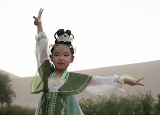 A cheerful young girl twirling in a vibrant, traditional peacock green lehenga with golden embroidery.