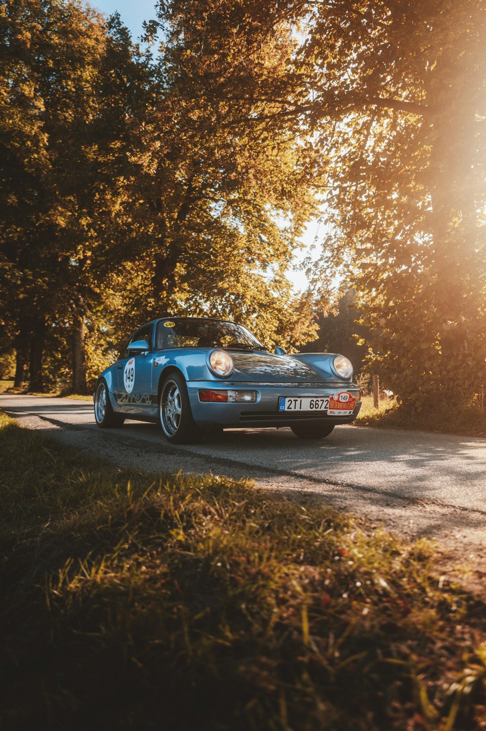 a blue car driving down a road next to a forest