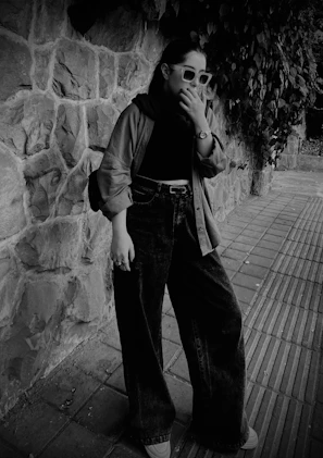A candid shot of a person adjusting their scarf in front of a textured brick wall, showcasing fabric details.